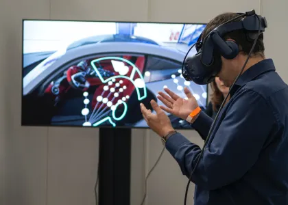 a man wearing a VR headset stands in front of a screen displaying the controls of an aircraft